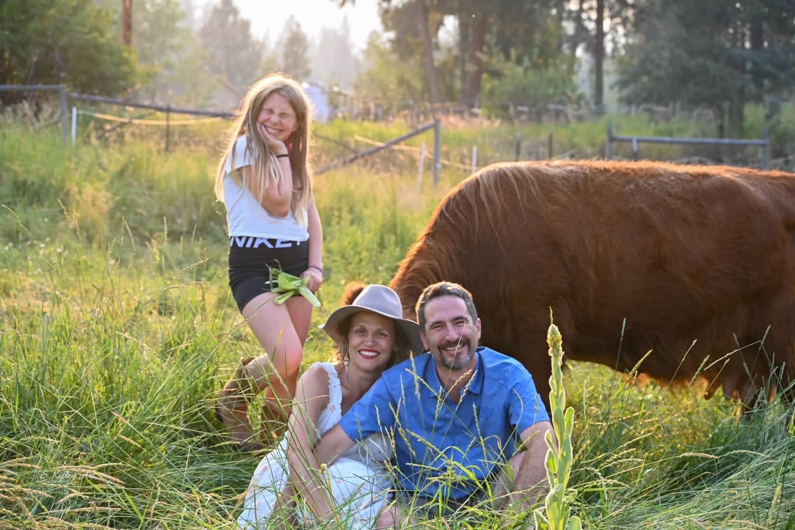 A family of four posed at the Highland-cattle pasture fence under soft overcast light — an example of one of the four standard session shapes the founding-family offer covers.